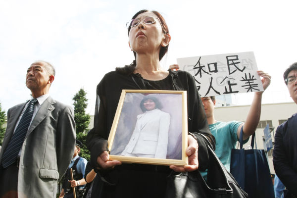 母親の祐子さんは娘の遺影を抱いて抗議に訪れた。後ろのプラカードは「和民 殺人企業」。＝写真：山田旬＝