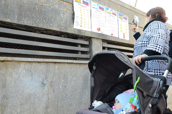 ロシアとウクライナの生活水準を比較した貼り紙広告を携帯電話の内蔵カメラで撮影する母親。＝州議会前・シンフェロポル　写真：筆者＝