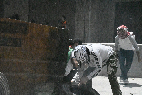 少年たちは鉄製の巨大ゴミ箱を弾除けにしながら前進して行った。＝14日、西岸側イスラエル国境　撮影：田中龍作＝