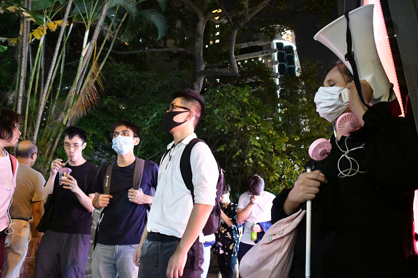国歌「願榮光歸香港」をトラメガで流す全盲の女性（右端）。8月11日、ここで救護班の看護師は機動隊に右目を撃たれ光を失った。＝10日夜、尖沙咀警察署前　撮影：田中龍作＝