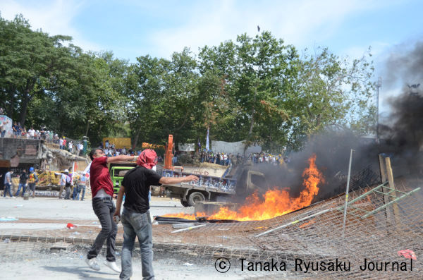 バリケードに火を放ち、機動隊に向かって投石するオキュパイの若者。＝11日午後3時頃（日本時間午後9時頃）、タクシム広場　写真：田中龍作＝