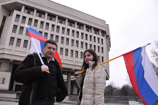 クリミア在住の同胞（左）を助けにモスクワから来たという女性。2人はロシアの国旗を誇らしげにかざしていた。後ろのビルはクリミア自治州議会。＝2日、州議会・州政府前広場　写真：筆者＝