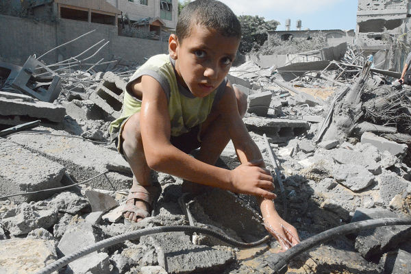 爆撃で破れた水道管から噴き出す水で体を洗う子供。＝24日、ジャバーリア　写真：筆者＝