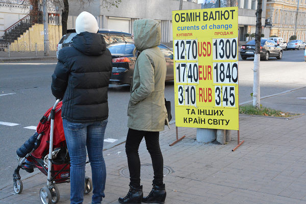 地元通貨のフリブナと対ユーロ、ドルの交換レートを表示する看板。ベビーカーを押す母親の背中がひと際寒そうだった。＝25日、キエフ市内 　写真：筆者＝