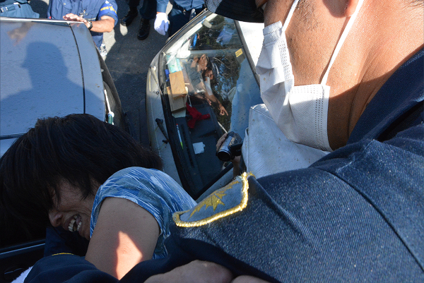 街宣車の上から落とされそうになり悲鳴をあげる女性。反対派住民のマイカーが下に見える。=22日午前8時50分頃、東村高江　撮影：筆者=