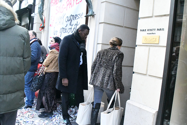 ブランド品で一杯の袋を下げた毛皮の女性（後ろ姿）はホテルの客だ。玄関は使えないため通用門から入って行った。＝20日、パリ・ハイアットホテル前　撮影：田中龍作＝
