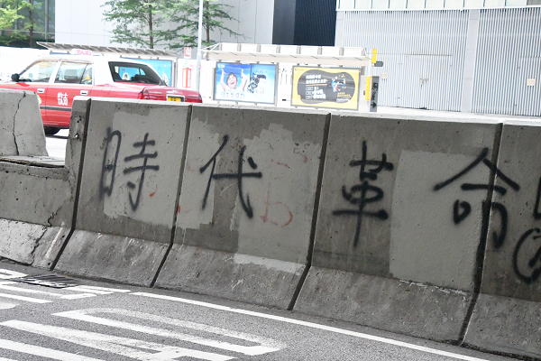 「革命」の文字が道路の分離帯にスプレーで書かれていた。場所は人民解放軍駐香港基地、政府本部庁舎の前だ。＝19日、金鐘　撮影：田中龍作＝
